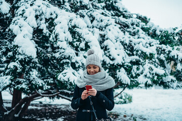 Beautiful young woman using smartphone and wearing scarf and a a hat on a cold winter day