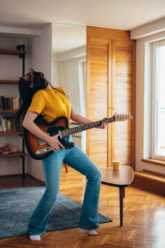 Woman Playing Guitar While Dancing And Singing In Her Living Room At Home