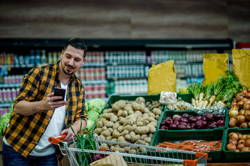 Young handsome man in a supermarket using smartphone while grocery shopping