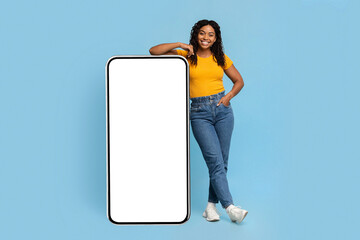 Happy black millennial lady standing by big cellphone, mockup