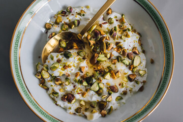 greek yogurt with green pistachios and honey in greek key bowl with gold spoon