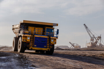 Industrial work in an open pit coal mine. A large yellow dump truck is carrying coal soil through...