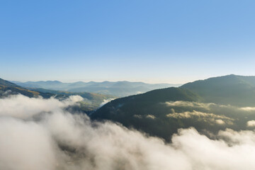 Aerial view of beautiful mountains covered with fluffy clouds on sunny day. Drone photography