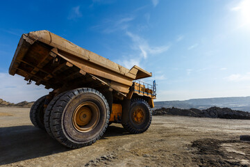 Fototapeta na wymiar Industrial work in an open pit coal mine. A large yellow dump truck is carrying coal soil through the quarry. Open pit coal mining.