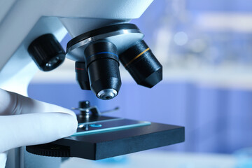 Scientist examining sample of light blue liquid on slide under microscope in laboratory, closeup