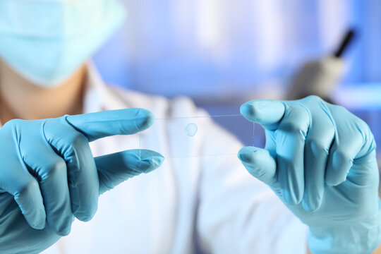 Scientist holding microscope slide with light blue sample in laboratory, closeup