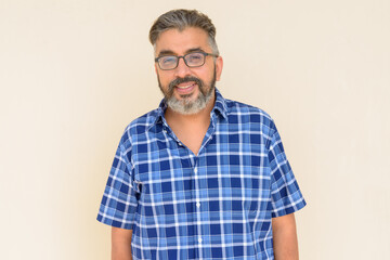 Portrait of bearded Indian businessman smiling against plain background