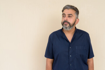 Portrait of bearded Indian businessman thinking against plain background