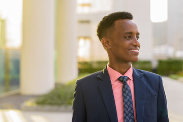 Portrait of happy young African businessman wearing suit and tie while thinking
