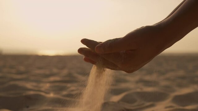 Close up. Hand woman releasing dropping sand through fingers in summer sunset 