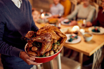 Close-up of man with Thanksgiving turkey during family dinner in dining room.