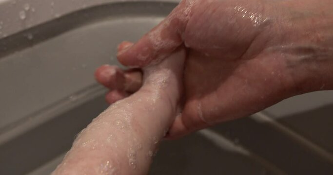 A parent bathes the child in a baby bath, soaping his feet. Close-up