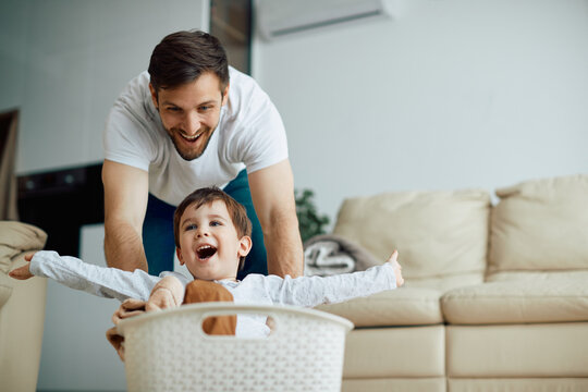 Carefree Boy Has Fun While Father Is Pushing Him In Laundry Basket Around The House.