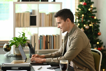 Obraz premium Side view smiling man working with laptop computer at home.