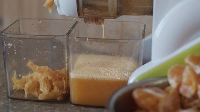 4K Close-up view of juice machine making homemade tangerine juice. Auger juicer working, pressing orange juice, making pulp. Squeezing process. Mandarins in metal bowl. Fruits for healthy breakfast