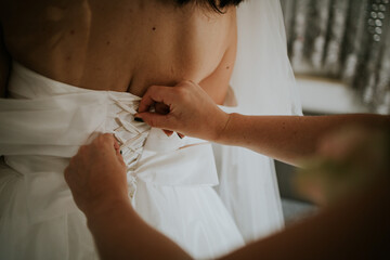 Closeup shot of a woman tying up the backside of the bride's dress at a wedding in Sarajevo