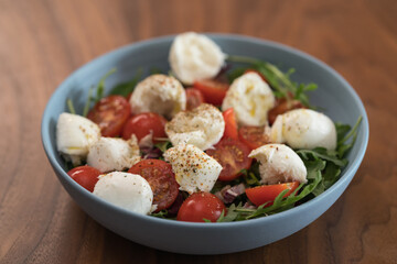 Salad with mozxarella, tomatoes and arugula in a blue bowl on walnut wood table
