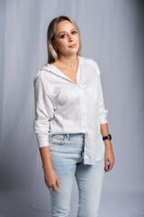 beautiful woman portrait in studio posing standing. girl in a white shirt and blue jeans, barefoot. blonde with straight hair and bright makeup. beauty concept. Gray background