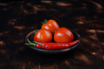 red chilies and fresh tomatoes on a tray with a dark wooden background