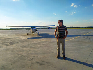 A young, handsome male pilot in casual clothes, glasses standing near a small pleasure plane on the...