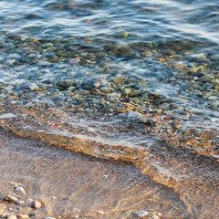 Background of sandy, stones and flowing waves on the sea beach. Summer holidays and coastal nature concept