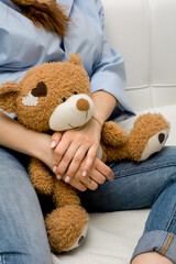 A pregnant woman hugs a teddy bear while sitting on the couch.