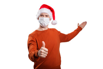 Fototapeta na wymiar an isolated shot of a happy man in a medical mask from the coronavirus, in casual clothes, an orange sweater, a Christmas hat. gesture ok, the other hand points back, looks into the camera