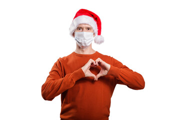 an isolated shot of a happy man in a medical mask, in casual clothes, an orange sweater, a Christmas hat. He shows his fingers to the heart, a gesture of love and health, looks into the camera