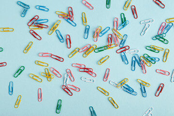 Multi-colored paper clips are on a light blue background. Paper clips are randomly arranged throughout the frame.