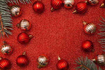 Obraz na płótnie Canvas Christmas decorative composition with fir branches, golden and red christmas balls on red shiny background. Christmas or New Year concept. Festive background with baubles and copy space.