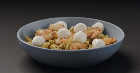 add mozzarella balls to pesto penne with shrimps in blue bowl on black background