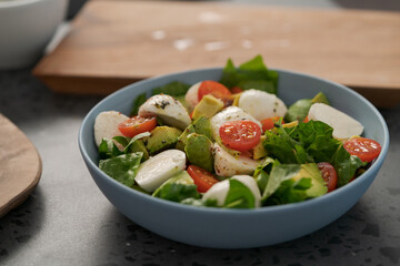 Salad with avocado, cherry tomatoes, romaine and mozzarella in blue bowl on concrete countertop