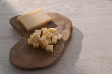 Small block of aged cheese sliced in small pieces on wood board