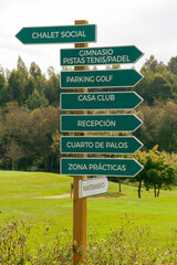 green signpost indianco the directions of the golf course, with a street in the background 