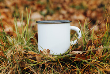 Metallic white mug mock-up. Hike camping or travel template concept. Close-up enamelled clean mug standing on autumn foliage outdoors