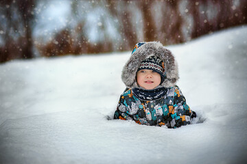 Fototapeta na wymiar cute caucasian boy in warm winther jacker with fur hoody laying in snow in countryside on winter day