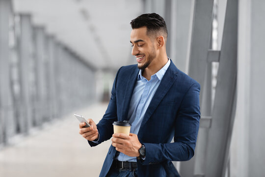 Young Arab Man Using Mobile Phone And Drinking Coffee In Airport