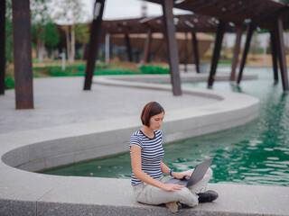 female student working with laptop in campus park.