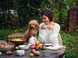 woman having breakfast in garden with her faithful pet poodle.