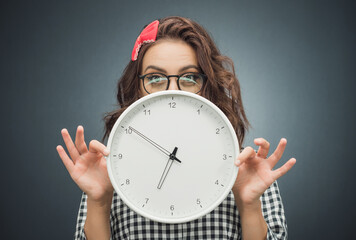 Astonished young woman with surprised face holding clock over dark gray - black background. Pretty...