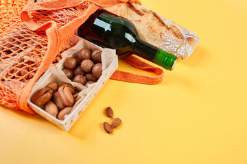 Flat lay Mesh grocery shopping eco friendly bag nuts, baguette and wine on yellow canvas background, Zero waste cconcept, Local farmers market, shopping mall, top view, copy space, Plastic free items.