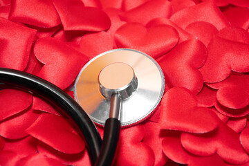 A stethoscope or phonendoscope lies on a large number of small red hearts: crop, medical cardiological concept, statistics of cardiovascular diseases

