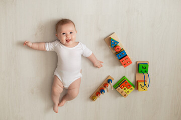 cheerful newborn baby in a white bodysuit lies on his back on the floor and plays with educational toys. products for children. concept of a happy childhood and motherhood. child care. space for text