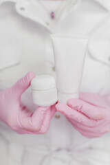 Beauty female doctor cosmetologist in medical gloves holding the bottle with lotion and presents an advertisement product. Model woman in medical robe isolated on white background