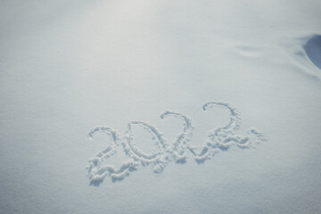 Drawing on white snow in sunlight. New Year's date, figures 2022, close-up.