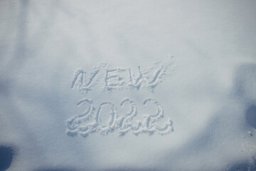 Drawing on white snow in sunlight. New Year's date, figures 2022, close-up. Winter holiday concept.