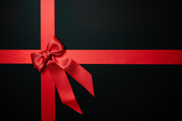 Red gift ribbon bow on black background. Table top view, flat lay, copy space.