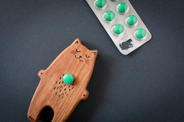 Wooden toy sleeping cat and blister of green pills on black background. Insomnia or sleep concept