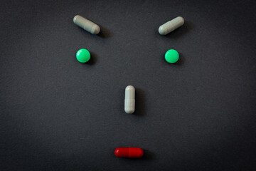 Creative emoticon, evil face of person realized with different tablets and pills of medicines on black background