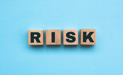 Word Risk made of small wooden cubes on blue background